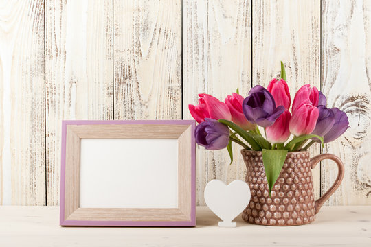 Fresh colorful tulips, white heart and blank wooden frame