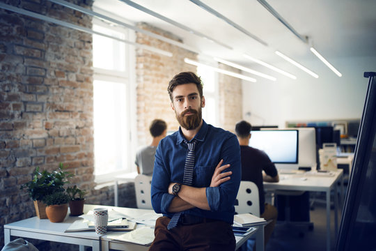 Man leaning on desk in office with colleagues in background