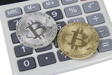 gold and silver bitcoin lies on a white calculator