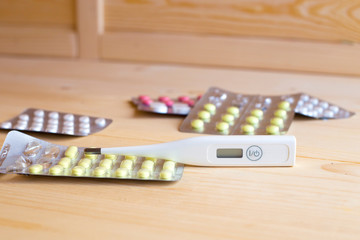 Disease. Medicines tablets and antibiotics with an electronic thermometer on the table
