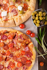 Rustic pizza with salami, mozzarellabasil top view with copy space. Two pizzas on a wooden table. Pizza salami on wooden background. Pizza salami with tomatoes and olives