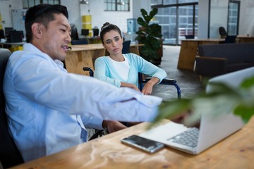 Businessman and disabled woman discussing over laptop