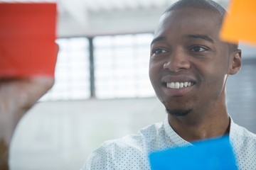 Smiling businessman reading sticky notes on glass