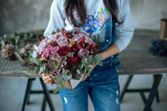 Woman florist in blue pants holds a bouquet of flowers hands in a wooden box