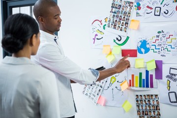 Graphic designers discussing over sticky notes on board