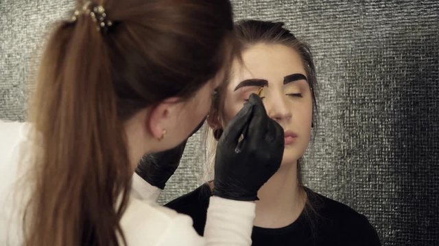 Makeup artist fixing the shape of painted eyebrows in salon