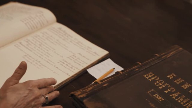 Close up shot of an old woman hands leaf through book russian cursive text on table