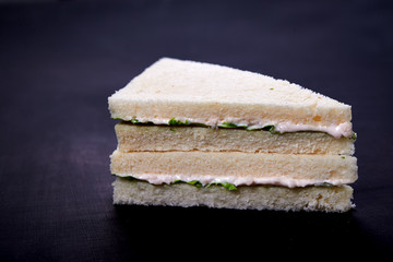 fish white bread sandwiches with salad leaves on dark wooden background