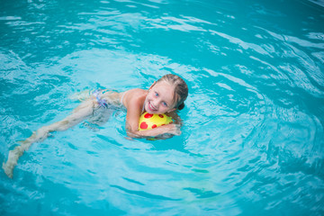 Fototapeta na wymiar Portrait of cute happy little girl having fun in swimming pool. Kids sport on family summer vacation. Active healthy holiday 