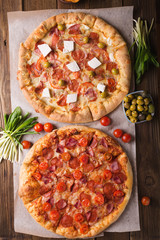 Rustic pizza with salami, mozzarellabasil top view with copy space. Two pizzas on a wooden table. Pizza salami on wooden background. Pizza salami with tomatoes and olives