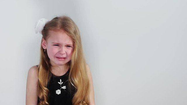 Beautiful crying little girl in black dress on the white background. 