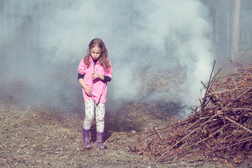 Girl in the garden with pile of dried branches in fire. Village life, countryside, tourism