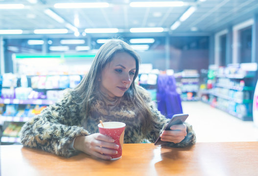 Woman using app on smartphone and drinking coffee in cafe