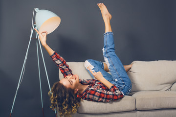 Close up portrait happy woman sitting on sofa.indoor portrait,young hipster girl,curly hair,paid shirt,blue jeans,girl thinking,positive emotions,red earrings,pretty face,face care,beauty make up.