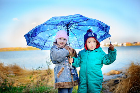 Little girl and boy with umbrella playing in the rain. Kids play outdoor by rainy weather in fall. Autumn fun for children. Toddler kid in raincoat and boots walk in the garden.