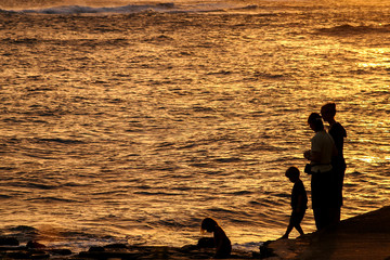 A silhouetted group of four enjoy the sunset at the beach in Kauai, Hawaii