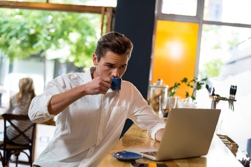 Man having coffee while using laptop