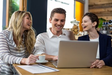 Happy friends interacting while using laptop