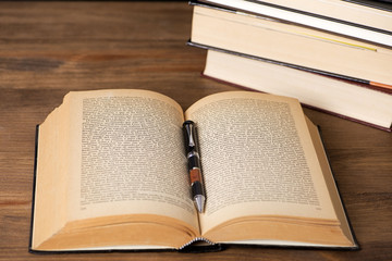 Open book with a pen on top next to several stacked books. Antiquity.