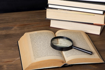 Close-up of an open book with a magnifying glass over it next to several stacked books.