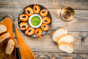 Seafood. Shellfish. Fried grilled shrimp prawns on a plate, with a sauce of olive oil and fresh herbs, with fresh baguette and a glass of wine. Snack, appetizer. On wooden table, top view, copy space