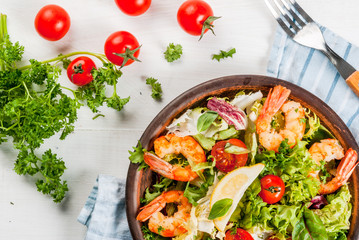 Seafood. Shellfish. Fresh lettuce salad with tomatoes, herbs and grilled fried shrimps prawns, on white table, top view, copy space