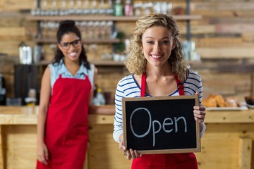 Smiling waitress standing with open signboard in cafe