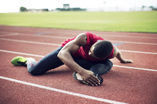 Sportsman sitting on running track and stretching