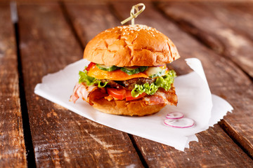 Burger piled with fresh toppings on whole-grain artisan buns, on a rustic wooden surface with a dark background