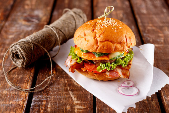 Burger piled with fresh toppings on whole-grain artisan buns, on a rustic wooden surface with a dark background