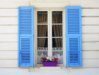 Vintage window with blue shutters on the background of a beige house. Vintage window with flower pot