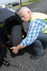 aged man changing leaking tire on the verge