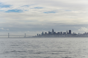 A cloudy sunset over the San Francisco bay seen from a boat on the water. Views of the city and golden gate bridge