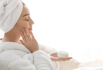 Obraz na płótnie Canvas Beautiful young woman applying cream onto skin in spa salon