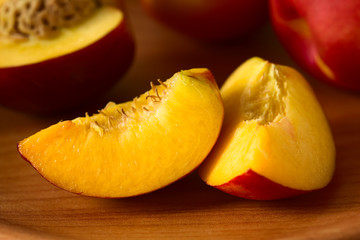 Slices of fresh ripe nectarine fruits on wooden plate, photographed with natural light (Selective Focus, Focus on the front of the left slice)