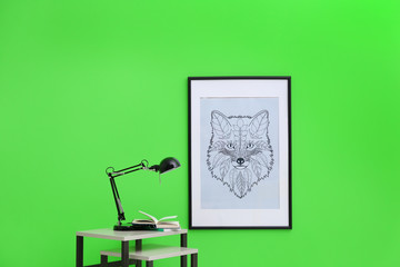 Books and lamp on table near green wall with painting