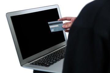 Mid section of hacker using laptop and credit card