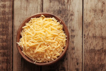 Bowl with grated cheese on wooden background