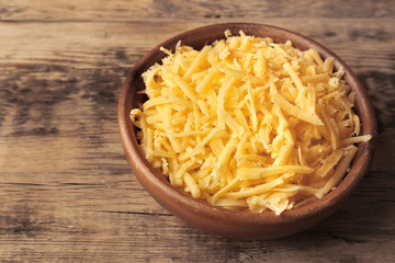 Bowl with grated cheese on wooden background