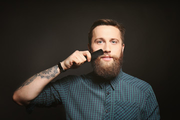 Portrait of handsome bearded man brushing mustache on black background