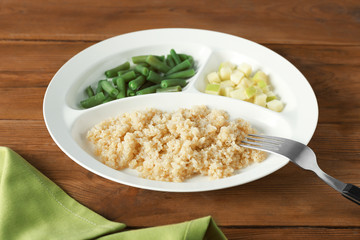 Plate with cooked quinoa on wooden table
