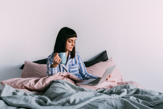 Hipster girl lounging in bed with coffee