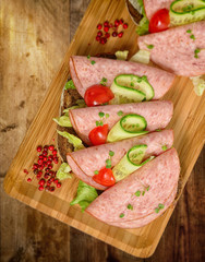 Open sandwich luncheon meat with cucumber and tomato on bamboo plank. Top down view.