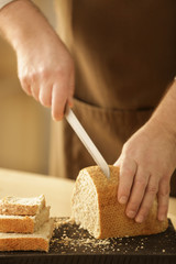 Hands of man cutting bread on kitchen table