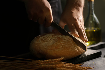 Man cutting bread on kitchen table, closeup