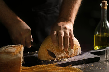 Man cutting bread on kitchen table, closeup