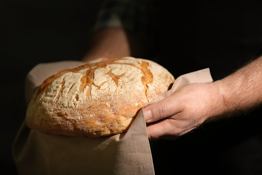 Male hands with loaf of bread on dark background, closeup