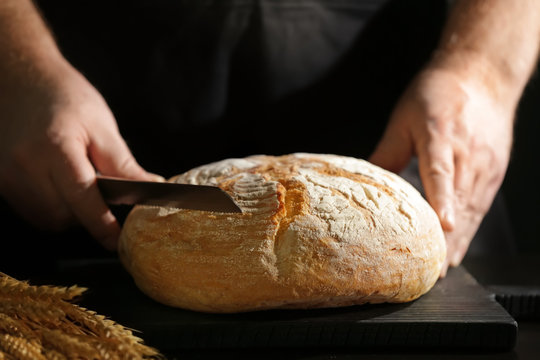 Man preparing to cut bread on kitchen table, closeup