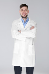 Young handsome pharmacist with crossed arms on grey background