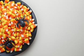 Plate with tasty Halloween candies on color background